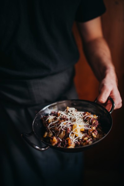 Eine Person h&auml;lt eine Pfanne mit Blunzengr&ouml;stl, garniert mit geriebenem K&auml;se.