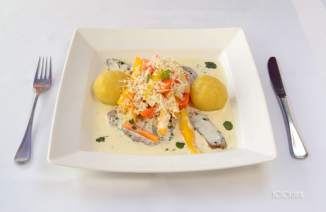 Ein Teller mit Krenfleisch, Kartoffeln und Gemüse in Sahnesoße.