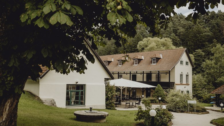 Ein idyllisches Wirtshaus mit Terrasse und Garten, umgeben von B&auml;umen.