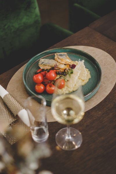 Ein Teller mit gegrilltem Fischfilet, Zitronenrisotto und Kirschtomaten, daneben ein Glas Wei&szlig;wein.