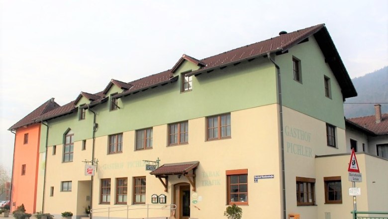 Ein zweistöckiges Gebäude mit der Aufschrift 'Gasthof Pichler', gelb und grün gestrichen, mit braunem Dach und mehreren Fenstern.