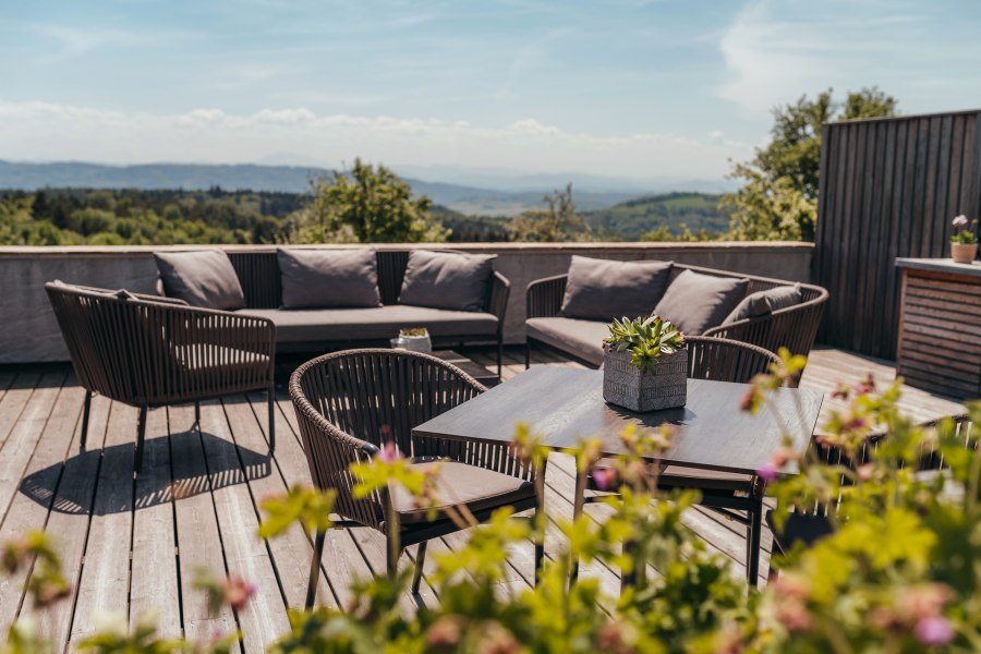 Terrasse mit Sitzm&ouml;beln und Pflanzen, im Hintergrund eine weite Landschaft.