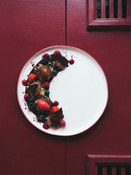Ein Dessertteller mit Schokoladen-Mousse und Beeren auf rotem Hintergrund.
