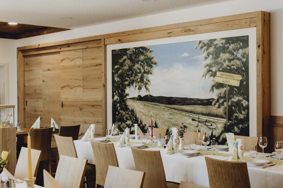 Innenansicht eines Wirtshauses mit gedecktem Tisch und Wandgem&auml;lde.