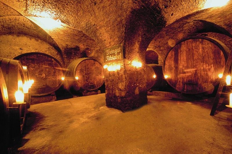 Historischer Weinkeller mit großen Holzfässern und Kerzenbeleuchtung.