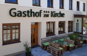 Fassade eines Gasthofs mit Holzpalettenm&ouml;beln vor dem Eingang.