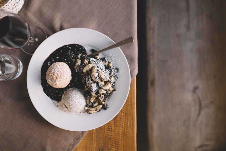 Ein Teller mit Mohnnudeln, Mohnknödel und Mohneis, dekoriert mit Puderzucker, auf einem Holztisch.
