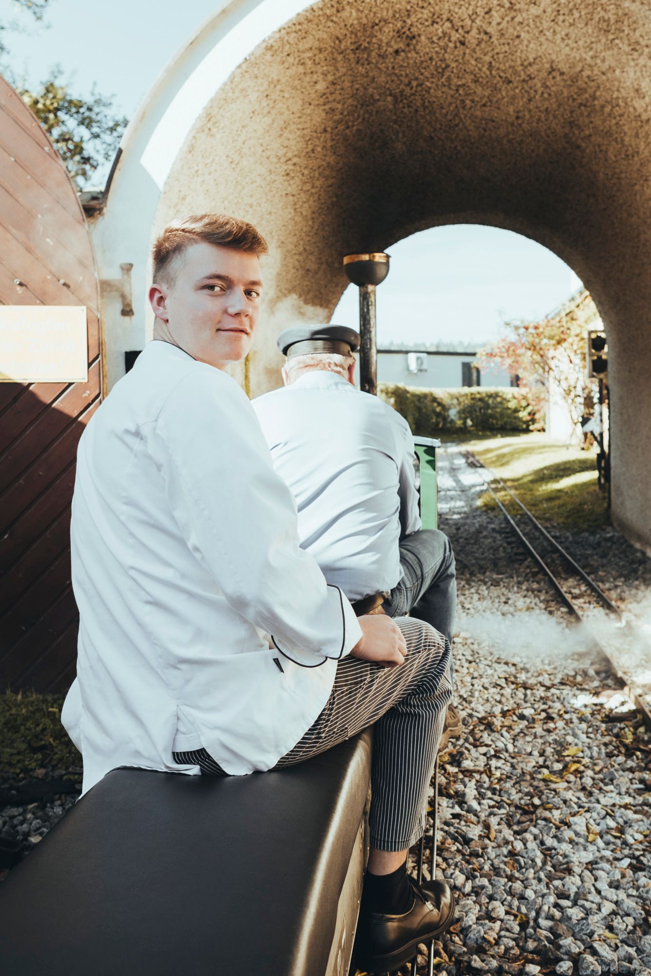 Zwei Personen sitzen auf einer dampfbetriebenen Minibahn, die durch einen Tunnel fährt.