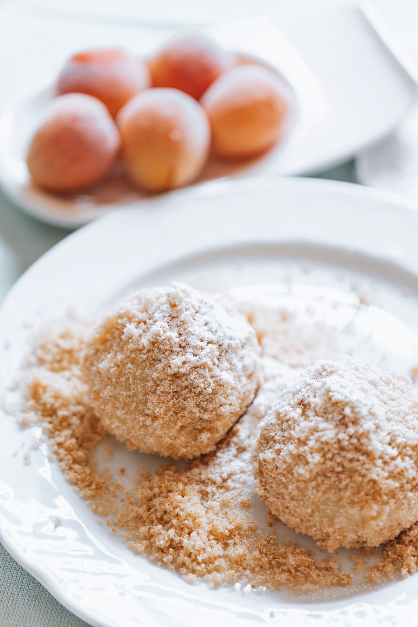 Zwei Marillenknödel mit Zucker bestreut auf einem Teller, im Hintergrund Aprikosen.