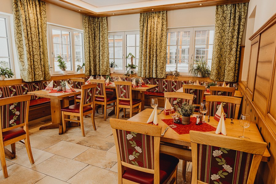 Gem&uuml;tliches Restaurant mit Holzm&ouml;beln, dekorierten Tischen und Pflanzen am Fenster.