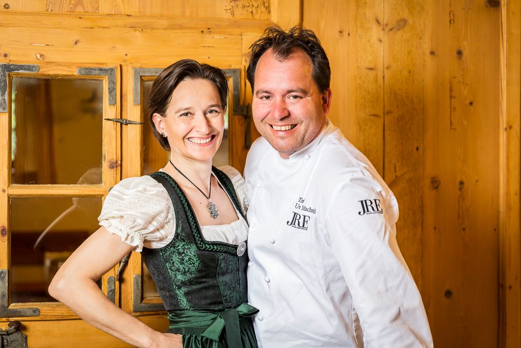 Ein Mann in Kochjacke und eine Frau in traditioneller Tracht lächeln in die Kamera.