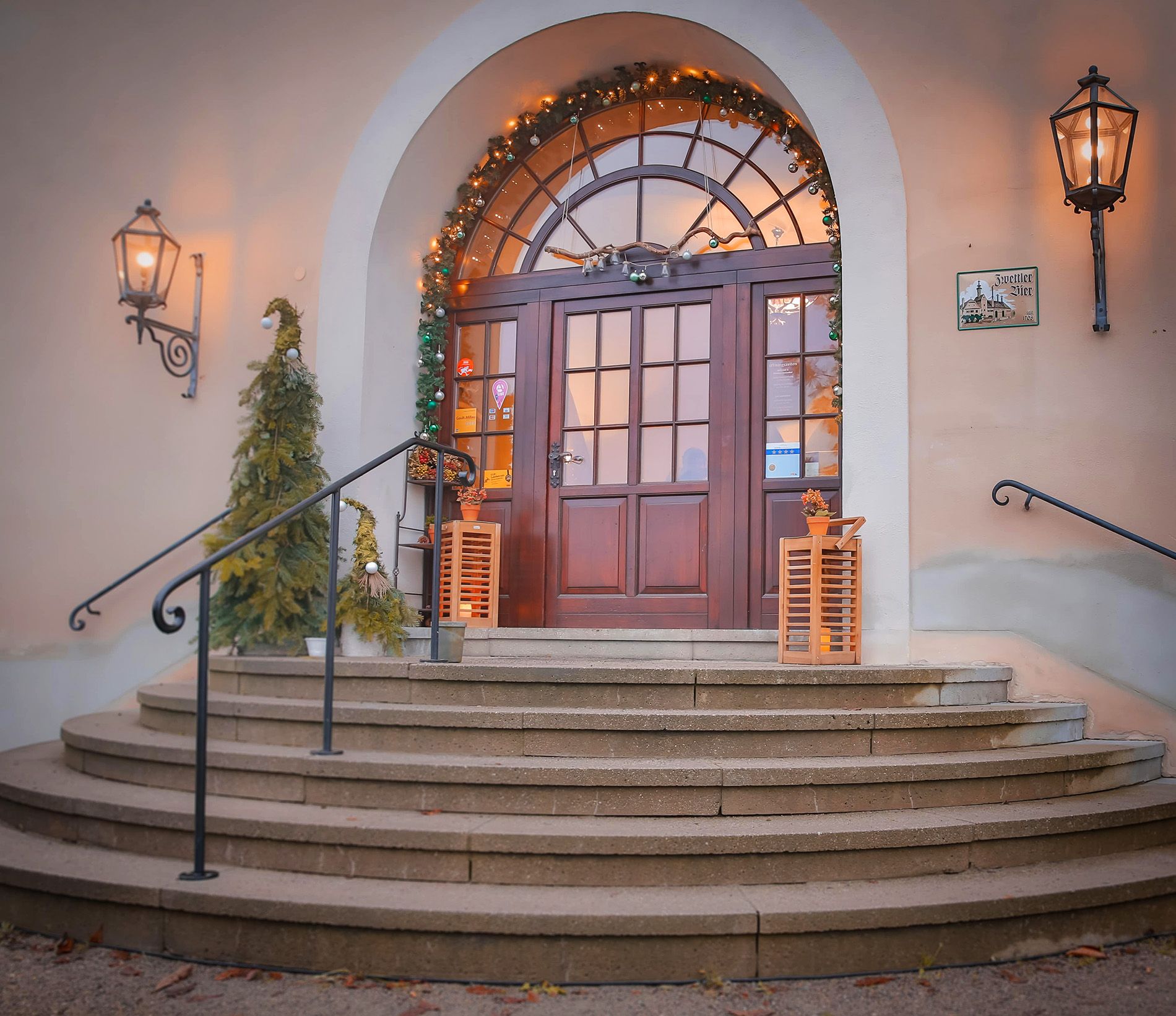 Eingang mit dekorierten Weihnachtsbäumen und Lichtern.