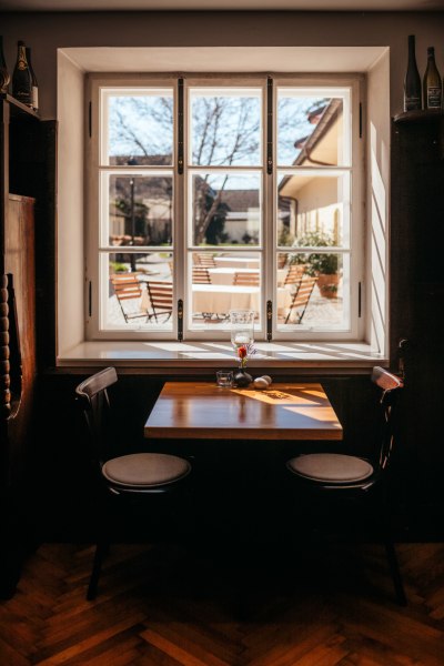 Ein Tisch mit zwei St&uuml;hlen vor einem Fenster, das einen Innenhof mit Tischen und St&uuml;hlen zeigt.