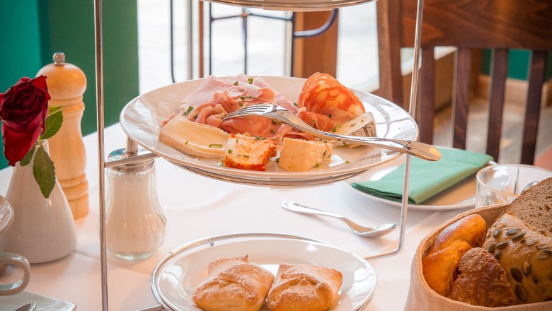 Ein Fr&uuml;hst&uuml;ckstisch mit einer Etagere voller Aufschnitt, Marmeladen und Br&ouml;tchen, daneben ein Glas Orangensaft.