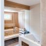 Innenansicht einer modernen Sauna mit Holzverkleidung und Glaswand, daneben eine wei&szlig;e Badewanne.