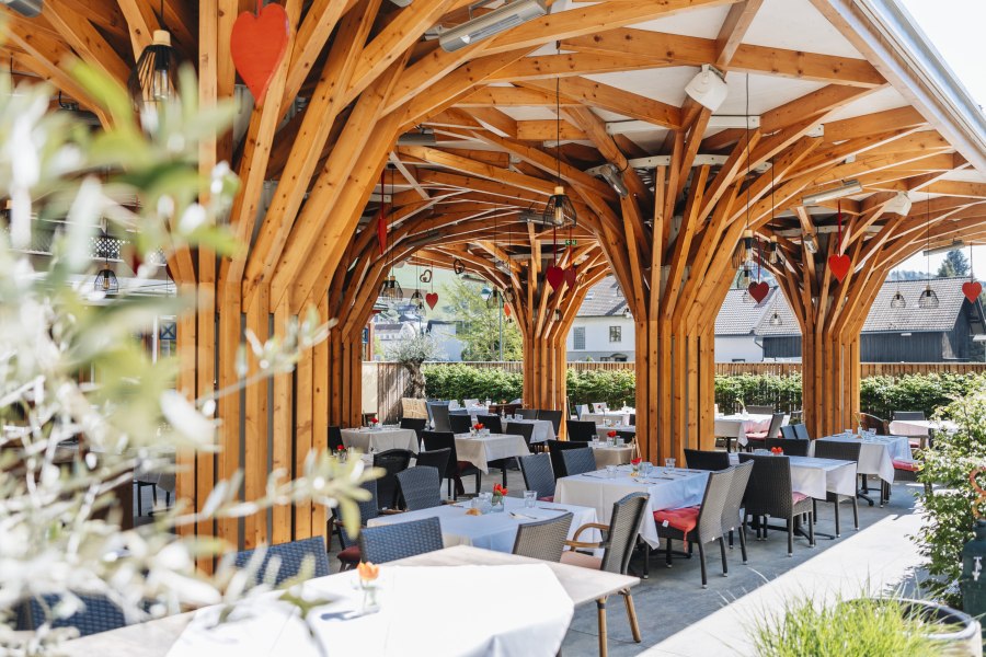 Moderner Gastgarten mit Holzkonstruktion und gedeckten Tischen.