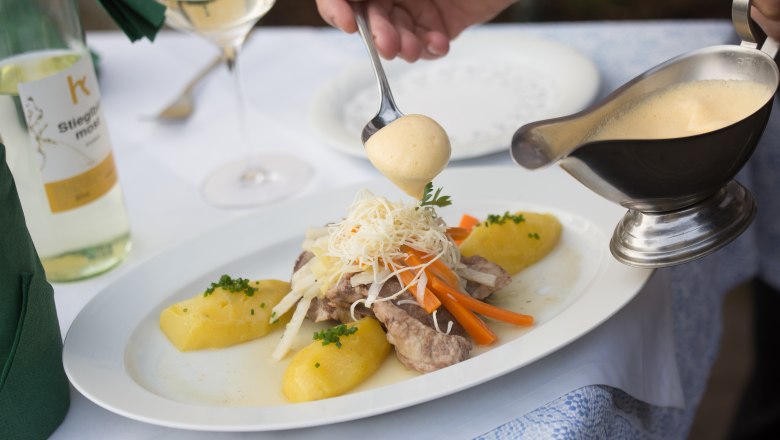 Ein Teller mit Fleisch, Gemüse und Kartoffeln wird mit Sauce übergossen.