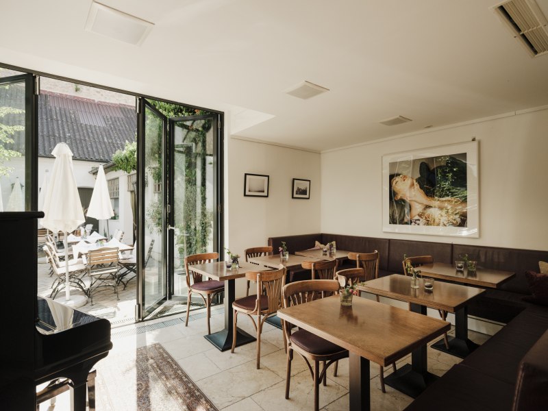 Gem&uuml;tliches Gastzimmer mit Holztischen, Kunst an der Wand und Terrasse im Freien.