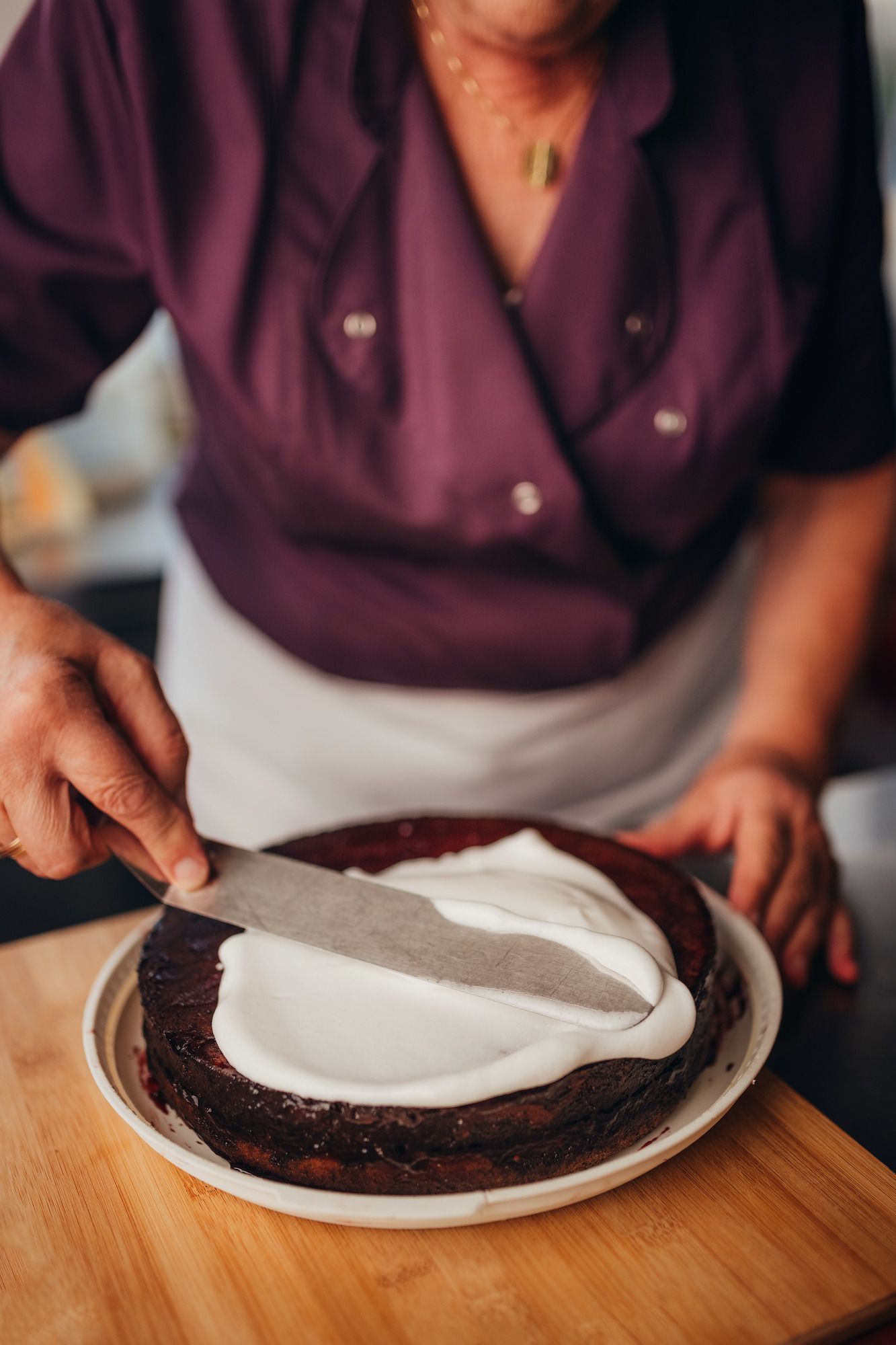 Eine Person streicht weiße Glasur auf eine Schokoladentorte.