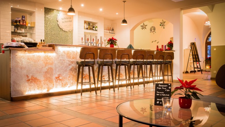 Elegante Bar mit beleuchtetem Tresen und hohen St&uuml;hlen, dekoriert mit Weihnachtssternen.