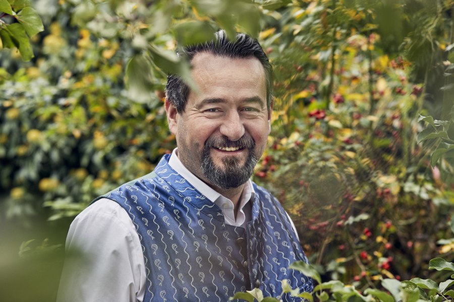 Ein Mann in traditioneller Kleidung lächelt in einem Garten.