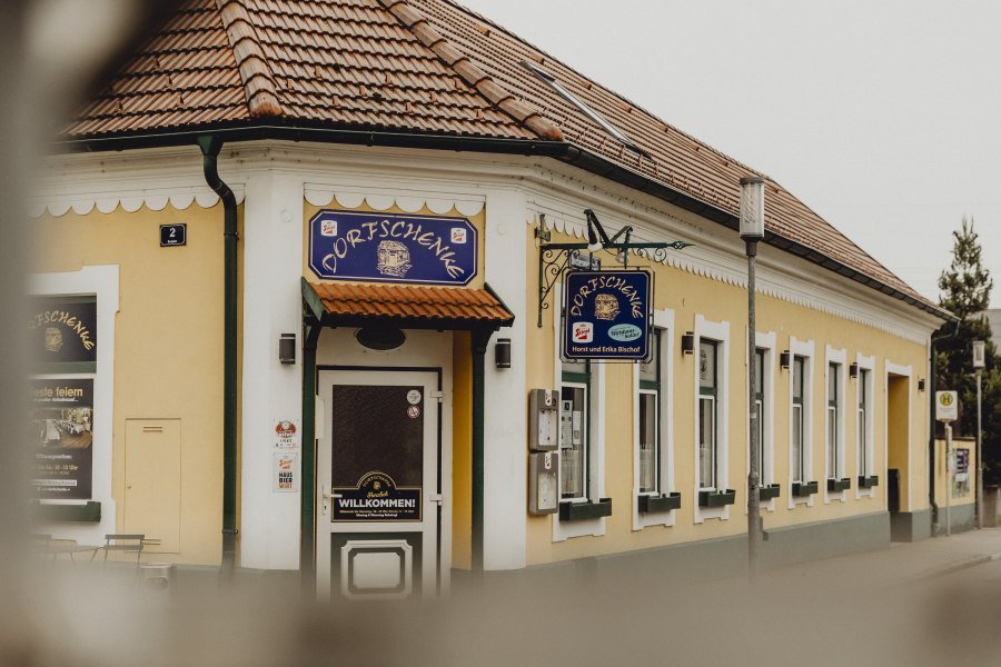Gelbes Gasthaus mit Schild 'Dorfschenke', traditionelles Ambiente.