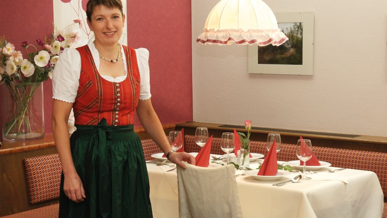 Eine Frau in traditioneller Kleidung steht neben einem gedeckten Tisch in einem Restaurant.