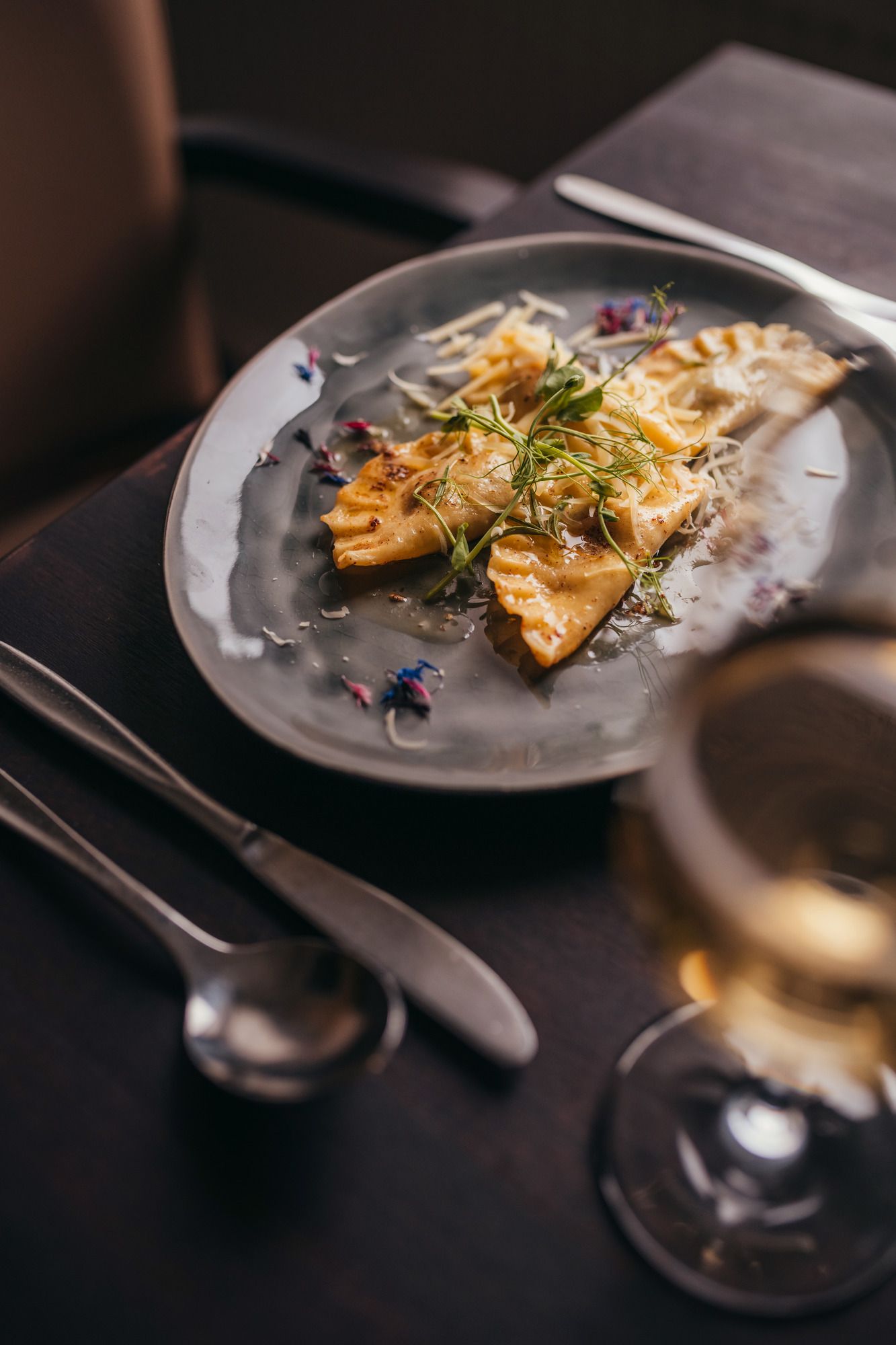 Elegante Ravioli auf grauem Teller mit Kräutern und Käse garniert.