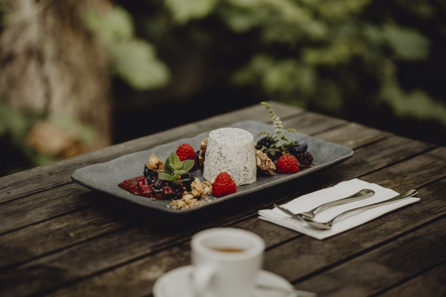 Mohn-Pannacotta mit Beeren und N&uuml;ssen auf einem Teller, serviert auf einem Holztisch im Freien.