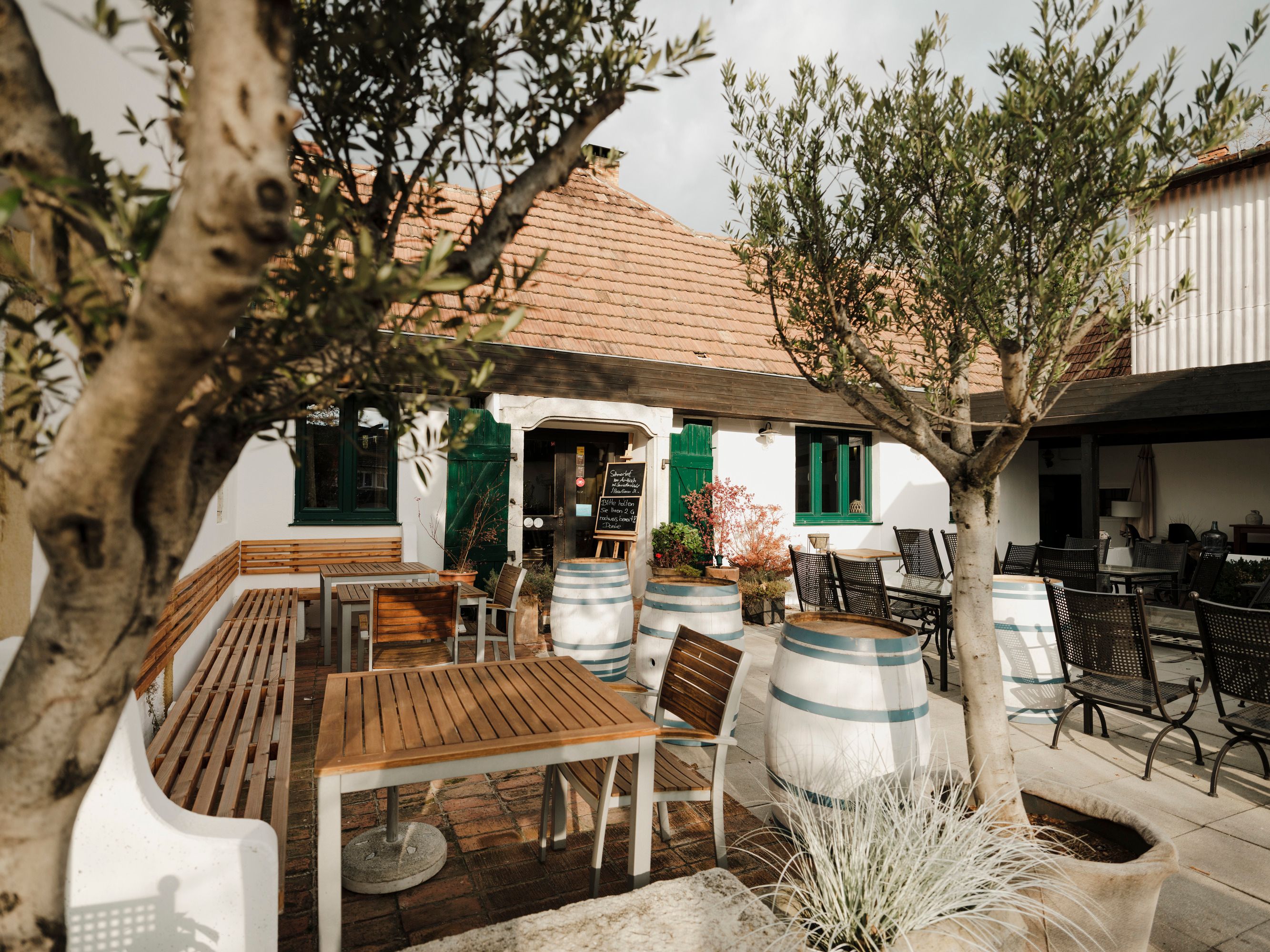 Gemütlicher Innenhof mit Holzmöbeln und Weinfässern, umgeben von Bäumen.