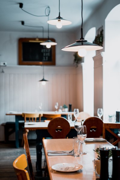 Innenansicht eines gem&uuml;tlichen Wirtshauses mit Holztischen, St&uuml;hlen und h&auml;ngenden Lampen.