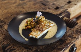 Gebratener Fisch mit Gemüsewürfeln und Sauce auf schwarzem Teller serviert.