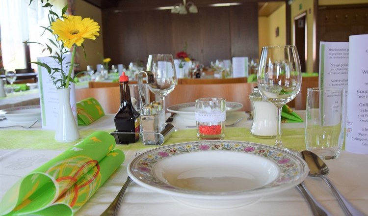Festlich gedeckter Tisch in einem Saal mit Blumen, Geschirr und Gl&auml;sern.