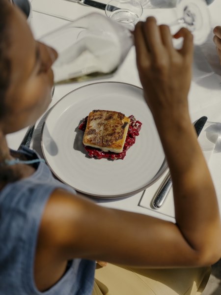 Person trinkt Wein zu einem Teller mit Fischgericht und roter Beilage.