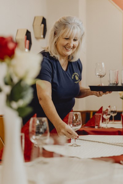 Frau deckt Tisch in einem Restaurant mit Weingl&auml;sern ein.