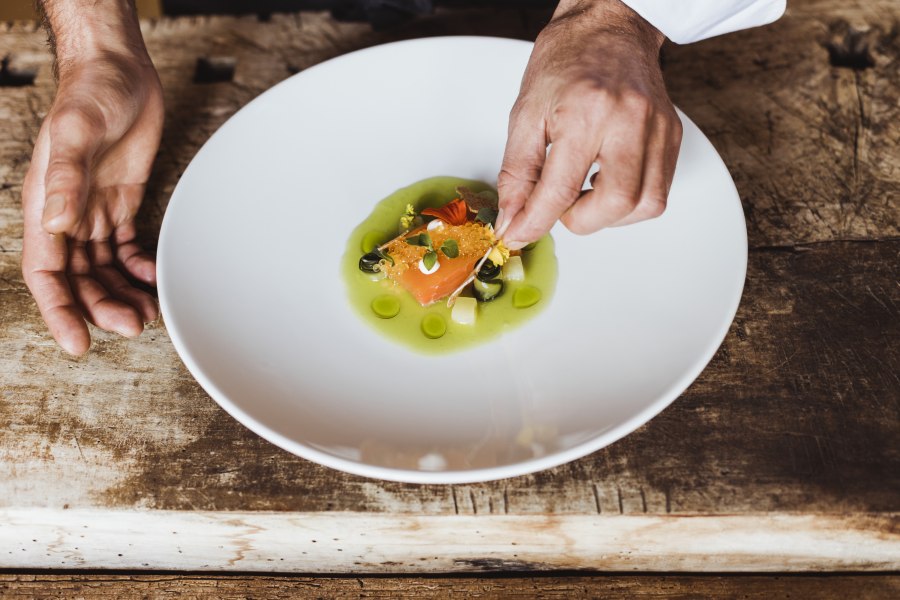 Ein Teller mit mariniertem Fisch und Kaviar, dekoriert mit grüner Sauce und Kräutern.