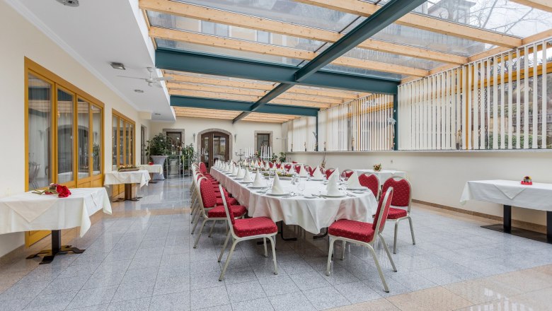 Eleganter Wintergarten mit gedecktem Tisch und roten St&uuml;hlen.