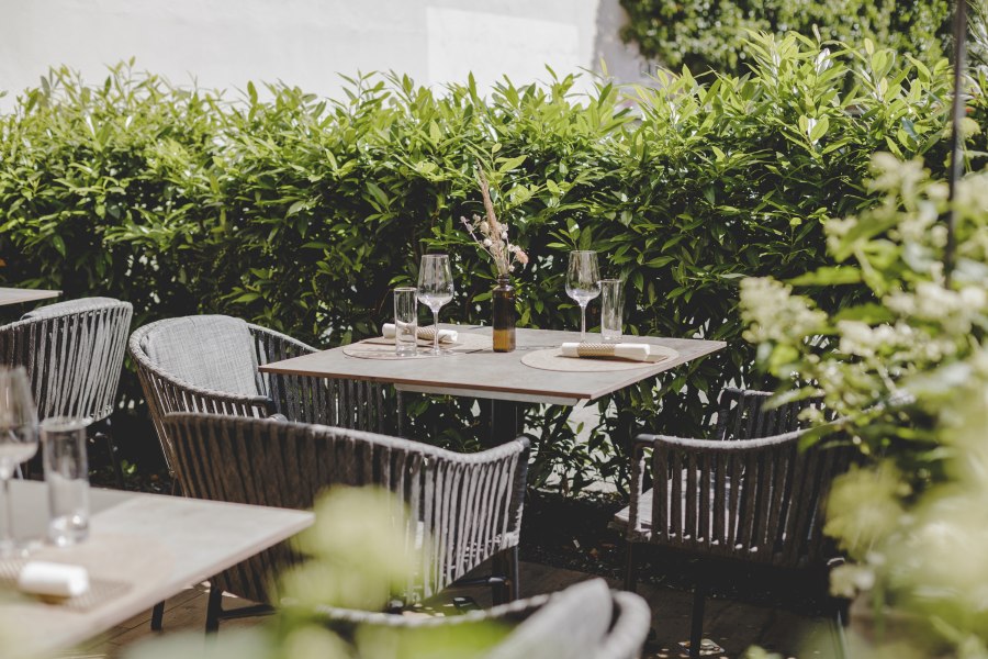 Ein gem&uuml;tlicher Gastgarten mit gedeckten Tischen und gr&uuml;ner Hecke im Hintergrund.