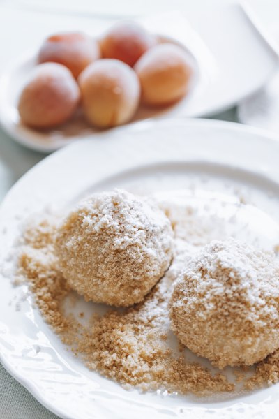 Zwei Marillenkn&ouml;del mit Zucker bestreut auf einem Teller, im Hintergrund Aprikosen.