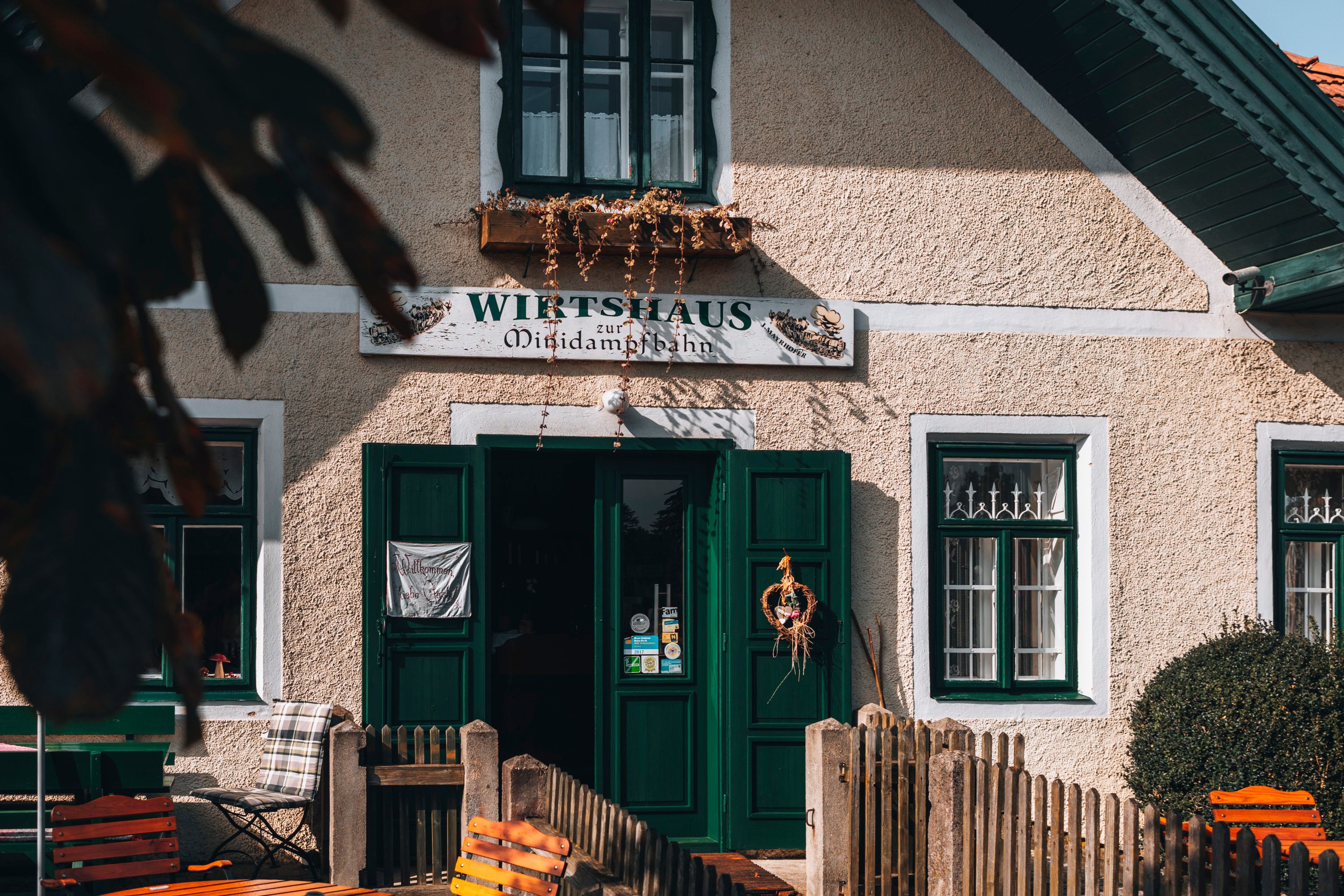 Eingang eines traditionellen Wirtshauses mit grünen Türen und Fenstern, dekoriert mit einem Kranz.