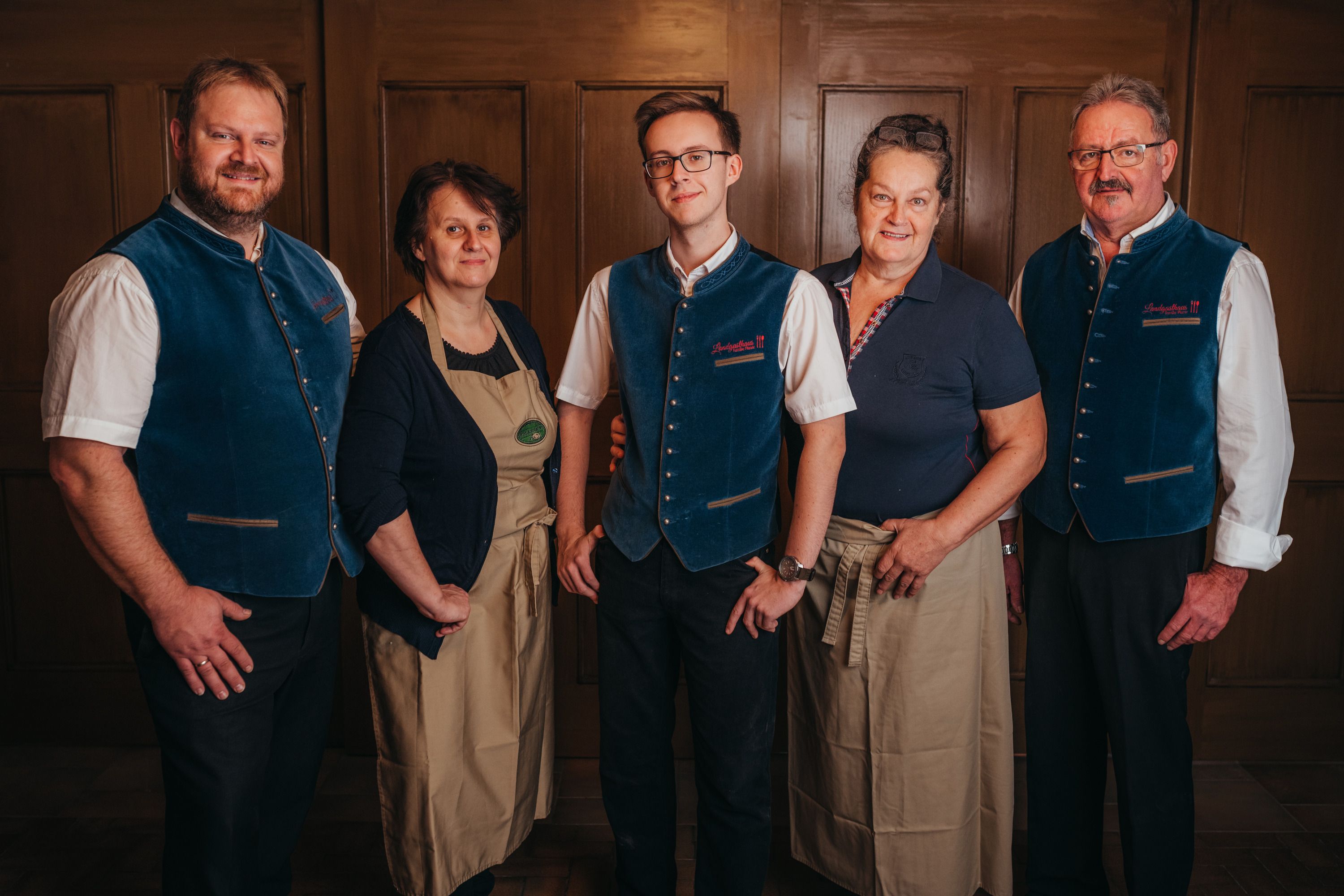 Fünf Personen in traditioneller Kleidung stehen vor einer Holzwand.