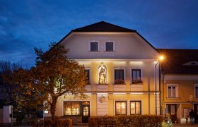 Gasthaus St. Florian bei D&auml;mmerung mit beleuchteter Fassade und Statue.