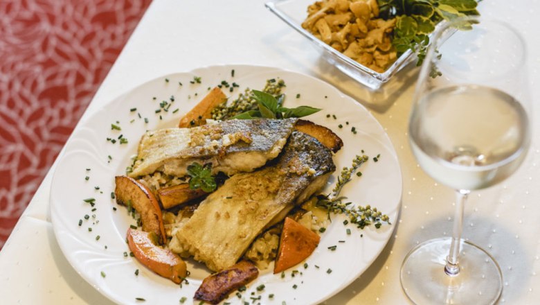 Gourmetgericht mit Fischfilet, Gem&uuml;se und Wei&szlig;wein auf wei&szlig;em Tisch.