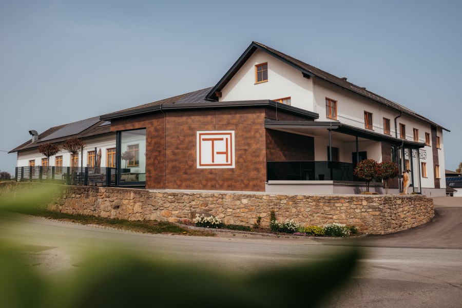 Ein modernes Geb&auml;ude mit der Aufschrift 'Gasthof Thaler', umgeben von einer Steinmauer und Pflanzen.