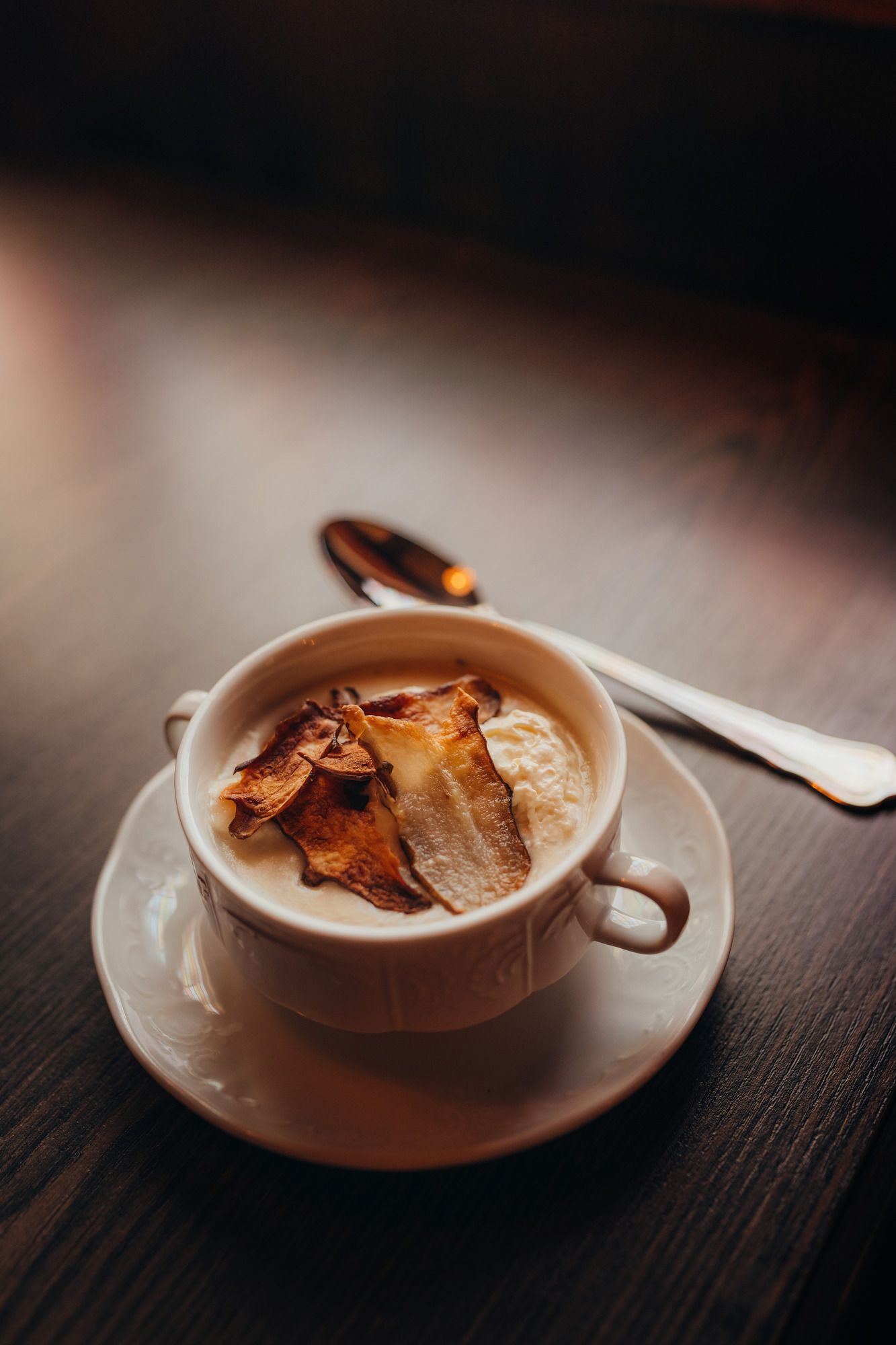 Eine Tasse mit Topinambur-Suppe, garniert mit knusprigen Chips, auf einem Holztisch.