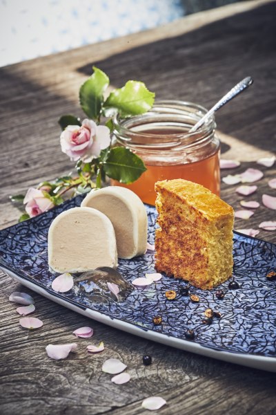 Ein Teller mit Entenleberparfait, Rosenblütengelee und Wacholder Brioche, dekoriert mit Rosenblüten und einem Glas Gelee im Hintergrund.