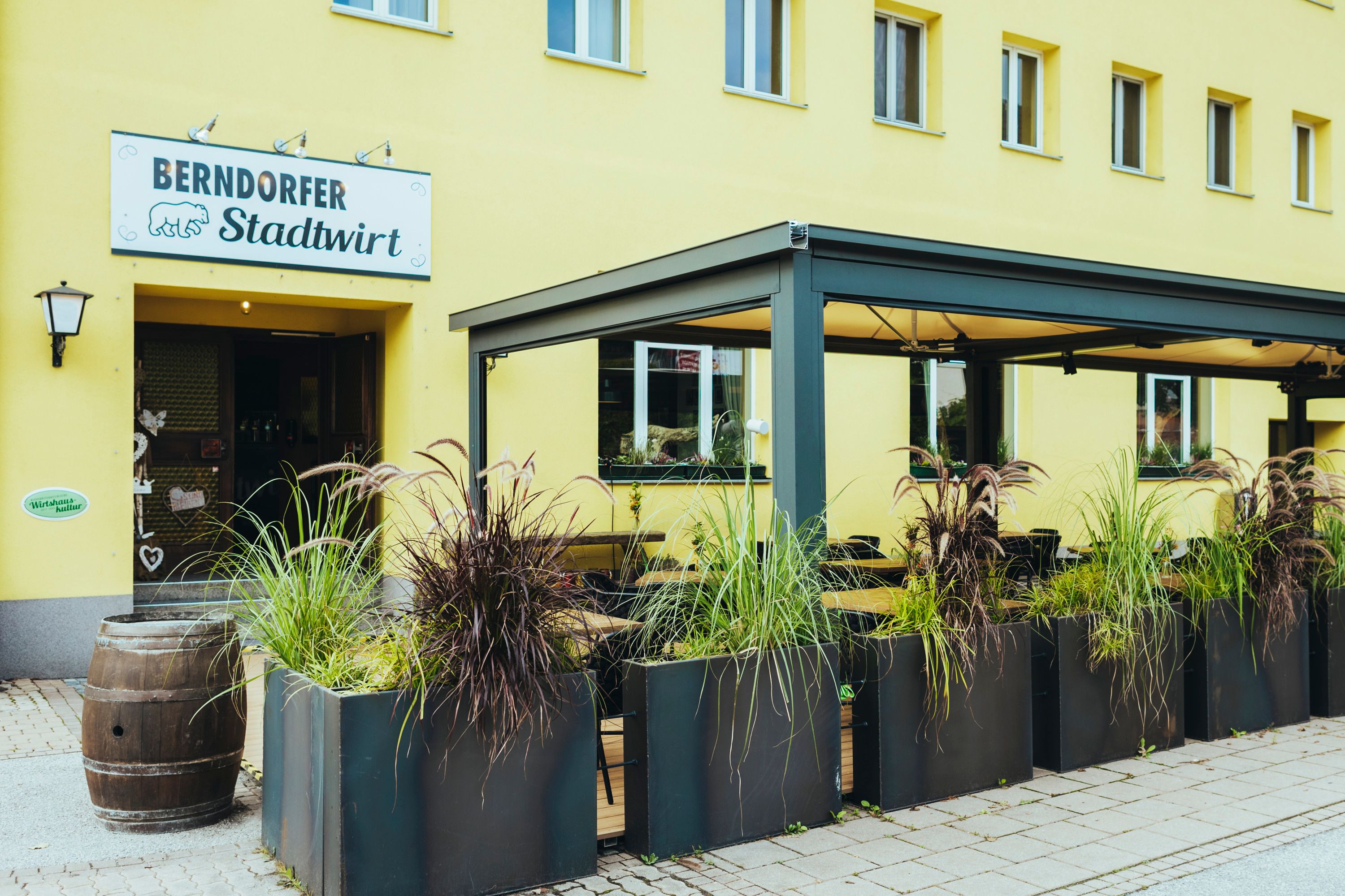 Eingang des Berndorfer Stadtwirts mit überdachtem Gastgarten und Pflanzen.