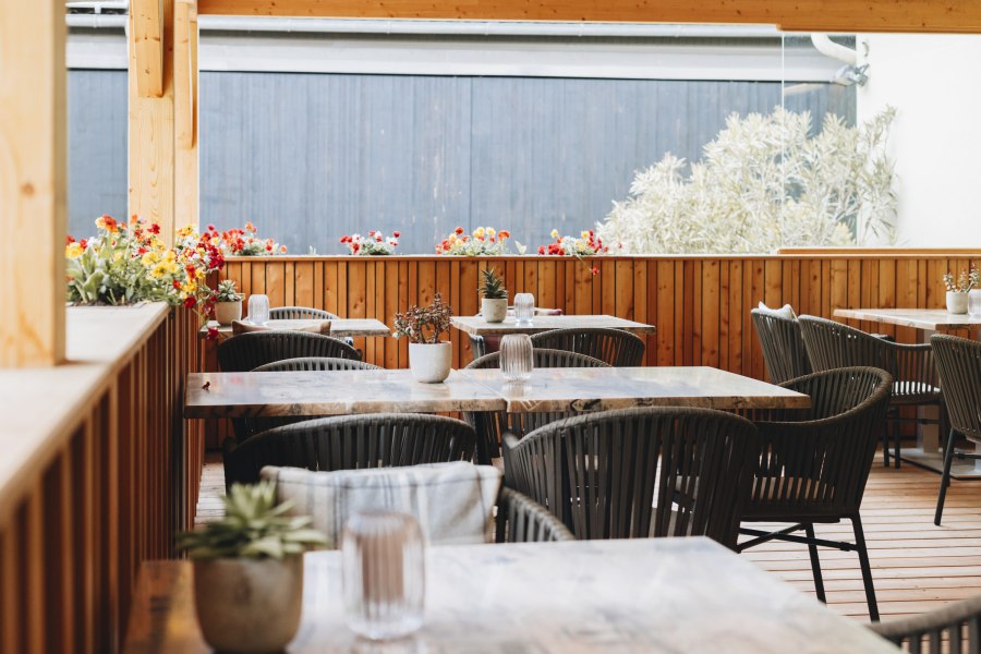 Ein gem&uuml;tlicher Innenhof mit Holzm&ouml;beln und Blumenarrangements auf den Tischen.