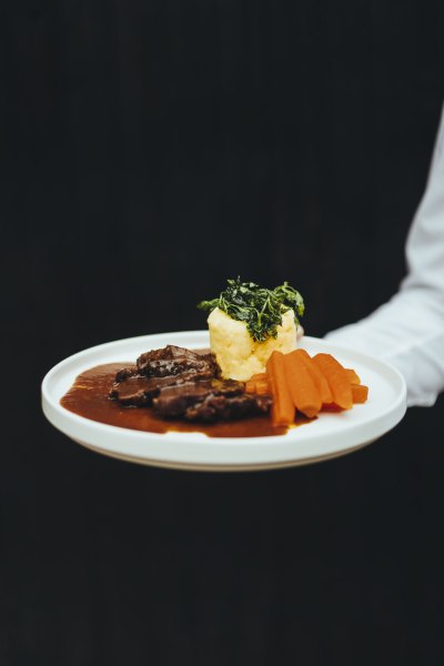 Gourmetgericht mit Fleisch, Karotten und Erd&auml;pfelstampf auf wei&szlig;em Teller.