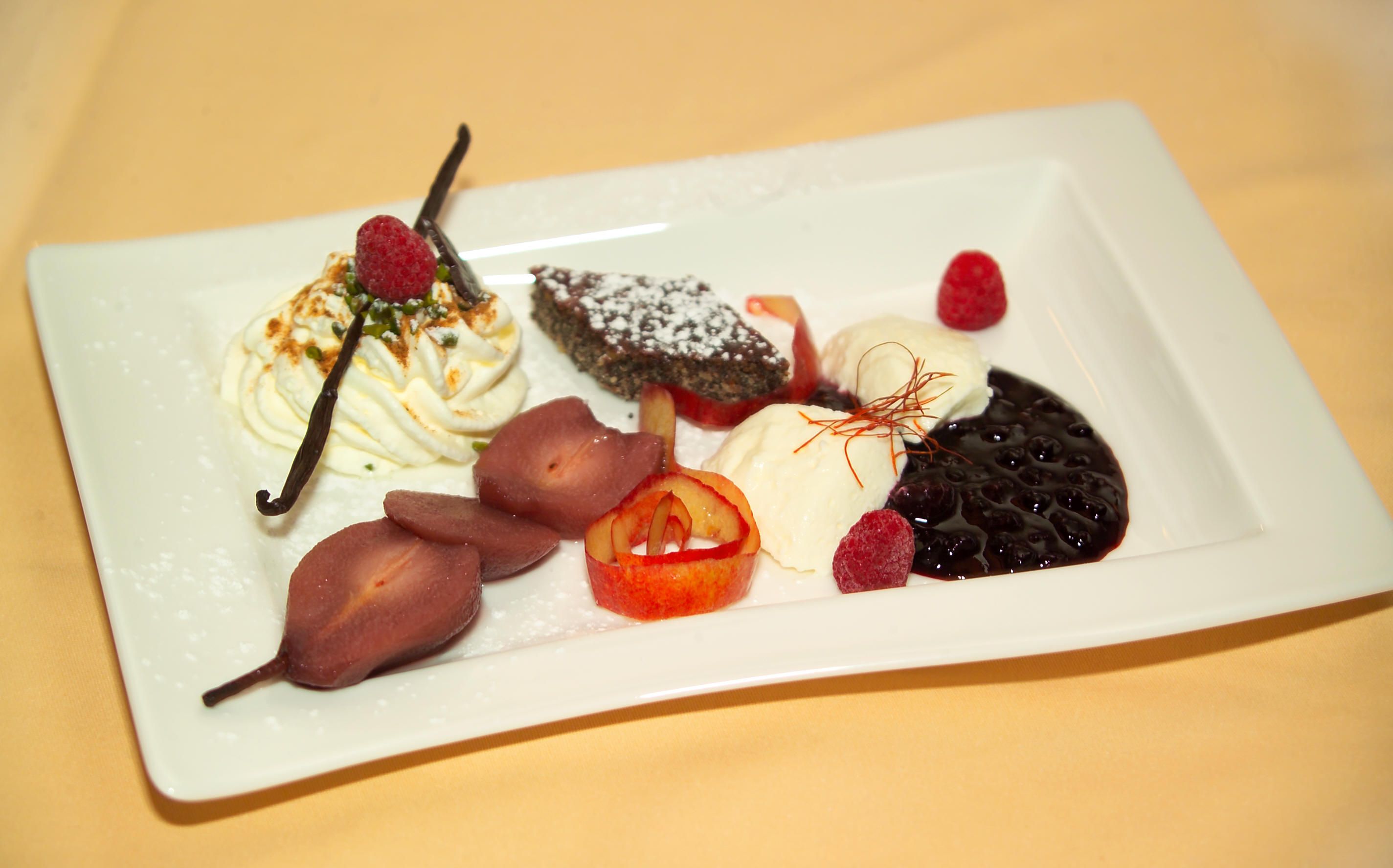 Ein Dessertteller mit verschiedenen Süßspeisen, darunter Sahne, Beeren, Schokoladenkuchen und pochierte Birnen.